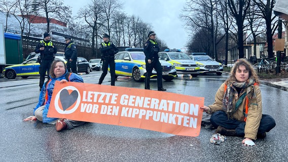 Aktivistinnen  der "Letzten Generation" sitzen mit einem Banner auf der Edmund-Siemers-Allee. © NDR Foto: Finn Kessler