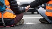 Klimaaktivisten der Gruppe "Letzte Generation" haben ihre Hände zusammengeklebt, um eine Straße  zu blockieren. © Bernd Thissen/dpa 