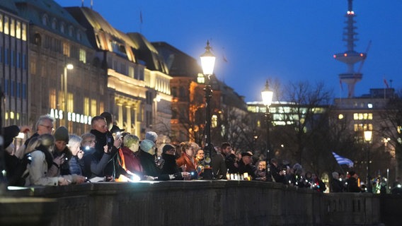Teilnehmerinnen und Teilnehmer halten ihre leuchtenden Handys und Taschenlampen während einer Kundgebung und Menschenkette gegen Rassismus an der Binnenalster hoch. © dpa-Bildfunk Foto:  Marcus Brandt