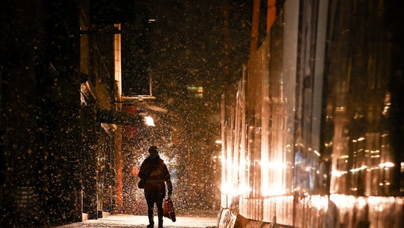 Eine Passantin geht bei leichtem Schneefall im Licht eines Schneeräumfahrzeugs die Hamburger Mönckebergstraße entlang. © dpa Foto: Christian Charisius