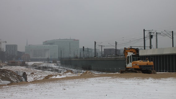 Ein Bagger steht auf einer weiten Sandfläche neben der Bahnstrecke in der Hafencity. © NDR Foto: Daniel Sprenger