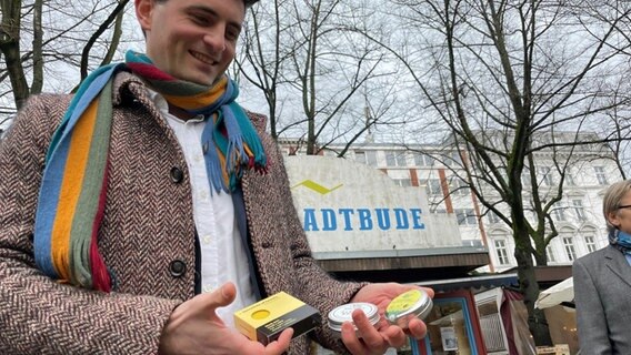 Ein Mann zeigt auf dem Hamburger Großneumarkt "Made-in-Hamburg"-Produkte für die Online-Plattform LOKL Hamburg. © NDR Foto: Jörn Straehler-Pohl