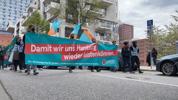 Demonstrierende tragen ein Banner mit der Aufschrift "Damit wir uns Hamburg wieder leisten können" bei der Maidemo "Hamburg enteignet". © NDR Foto: Screenshot