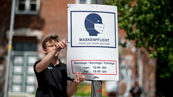 Ein Mann hängt in Hamburg ein Hinweisschild zur Maskenpflicht ab. © picture alliance / dpa Foto: Daniel Reinhardt