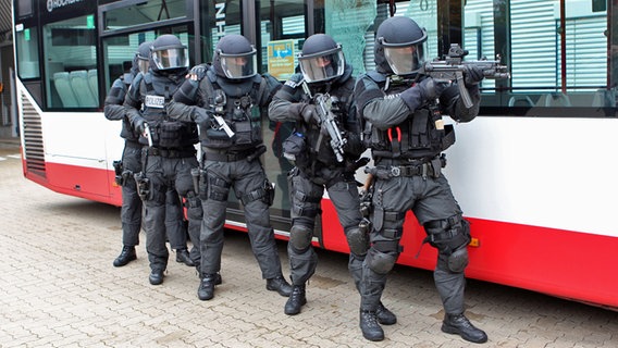 Fünf Polizisten des MEK Hamburg stehen hintereinander in voller Montur mit Gewehren im Anschlag an der Seite eines Buses. © Carolin Fromm/NDR Foto: Carolin Fromm