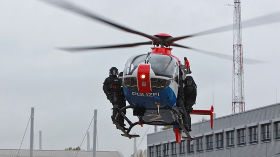 Zwei Polizisten stehen auf den Kufen eines fliegenden Helikopters. © Carolin Fromm/NDR Foto: Carolin Fromm