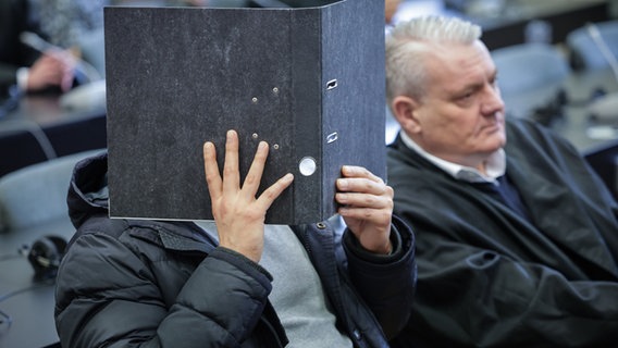 Der Angeklagte sitzt neben seinem Anwalt im Gerichtssaal im Strafjustizgebäude und verdeckt sein Gesicht mit einem Aktenordner © dpa-Bildfunk Foto: Christian Charisius