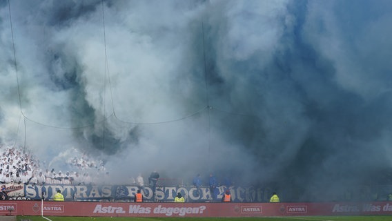 Los fanáticos de Hansa Rostock queman fuegos artificiales en las gradas.  © dpa Foto: Daniel Bockwoldt