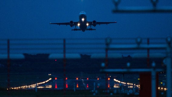 Ein Flugzeug über dem Hamburger Flughafen bei Dunkelheit. © picture alliance/dpa | Christophe Gateau 