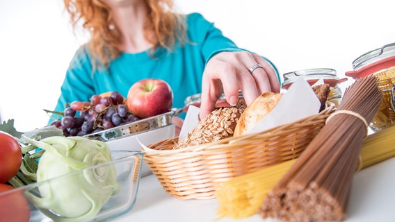 Eine Frau sitzt an einem Tisch mit verschiedenen Nahrungsmitteln. © picture alliance / dpa Themendienst Foto: Christin Klose