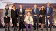 Bundeskanzler Olaf Scholz, die Holocaust-Überlebende Helga Melmed und weitere Gäste der Gedenkfeier in der KZ-Gedenkstätte Neuengamme in Hamburg bei einem Gruppenbild auf der Bühne. © dpa bildfunk Foto: Georg Wendt