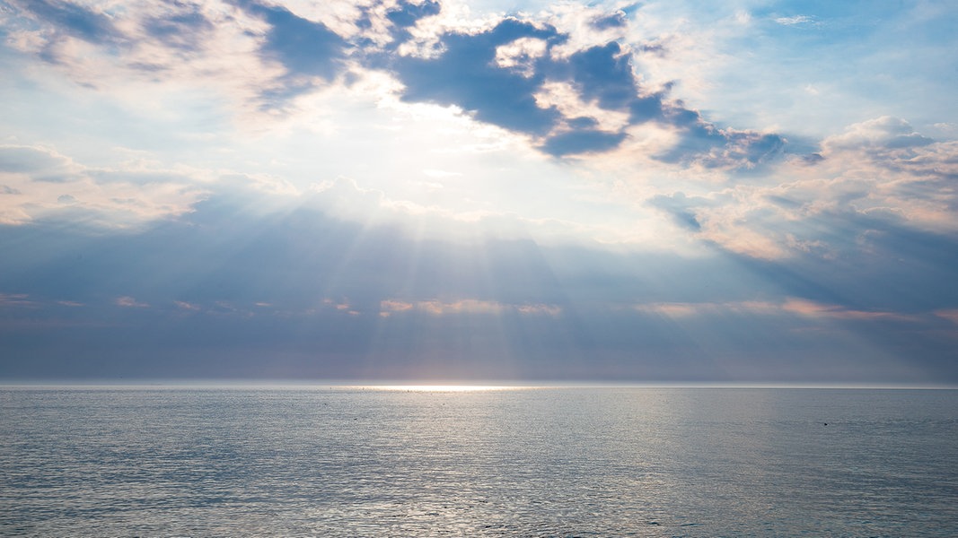 Sonnenstrahlen durchbrechen die Wolken über der ruhigen Nordsee vor Sylt.