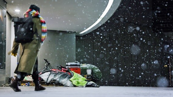 Eine Frau geht bei Schneetreiben in Hamburg an einem obdachlosen Menschen vorbei. © picture alliance/dpa Foto: Christian Charisius