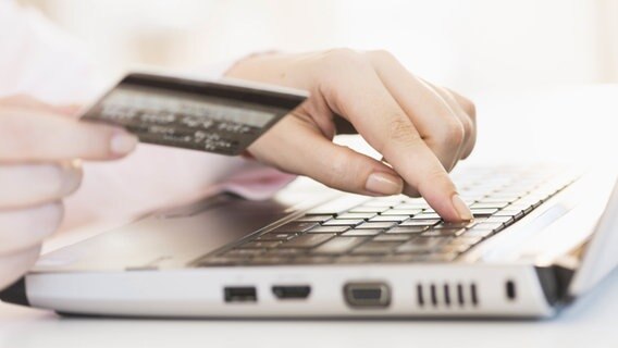 Eine Frau hält eine Kreditkarte in der Hand und tippt auf der Tastatur eines Laptops. © picture alliance/Bildagentur-online 