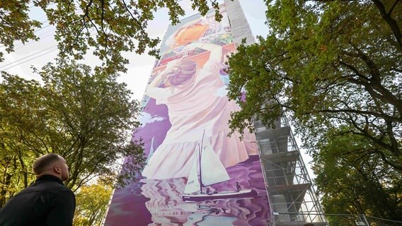 Eine Person betrachtet ein Wandbild an einer Fassade eines Hochhauses in Hamburg-Osdorf. © picture alliance/dpa Foto: Christian Charisius