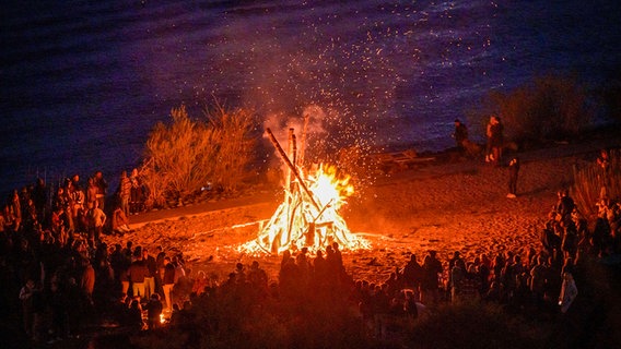 Mehrere Menschen stehen am Hamburger Elbstrand an einem Osterfeuer. © picture alliance/dpa Foto: Jonas Walzberg