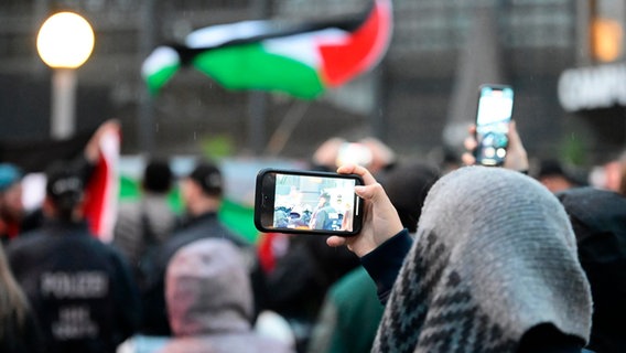 Teilnehmer einer pro-palästinensischen Kundgebung vor dem Hauptbahnhof tragen palästinensische Flaggen. © picture alliance/dpa Foto: Jonas Walzberg