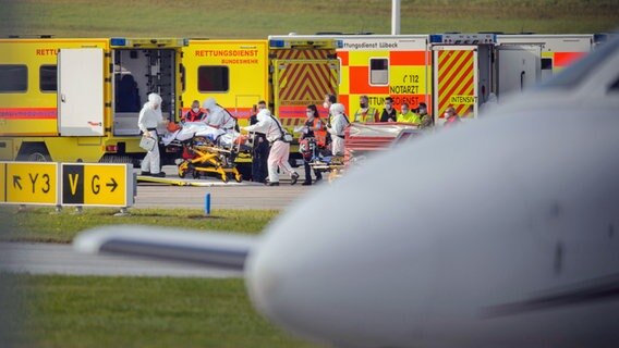 Medizinisches Personal in Schutzanzügen schiebt einen Corona-Intensivpatienten aus Rumänien auf einem Krankenbett in einen Rettungswagen der Bundeswehr auf dem Rollfeld des Flughafen Hamburg. © picture alliance/dpa Foto: Gregor Fischer