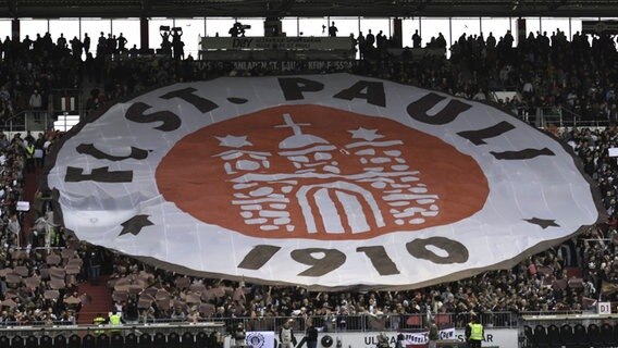 Ein überdimensionales FC St. Pauli-Logo wird von Zuschauerinnen und Zuschauern hochgehalten. © picture alliance / nordphoto GmbH/ Witke Foto: Witke