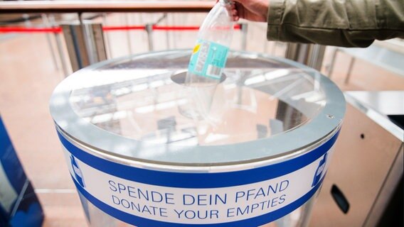 Eine Hand steckt am Hamburger Flughafen eine Flasche in eine Pfandspende-Tonne. © dpa Foto: Daniel Bockwoldt