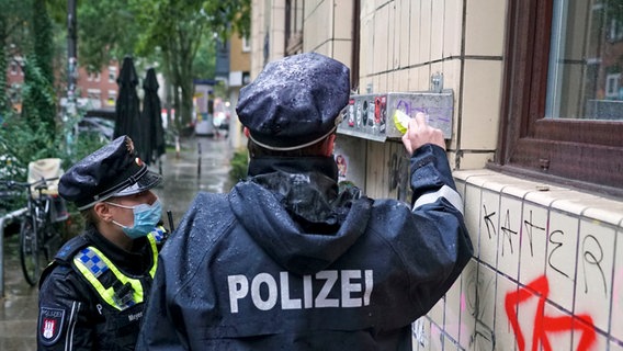 Polizisten entfernen einen Aufkleber mit den Worten "Andy, Du bist so 1 Pimmel" von einer Fensterbank in Hamburg. © picture-alliance 
