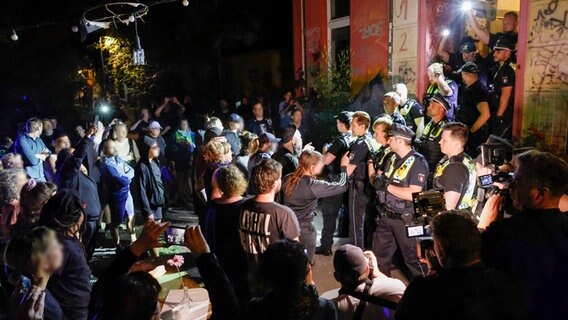 Menschen stehen zusammen vor der Polizei an einer Suppenküche im Hamburger Stadtteil St. Pauli. Bei einem Polizeieinsatz in einer Suppenküche im Hamburger Stadtteil St. Pauli sind drei Menschen verletzt worden, darunter zwei Beamte. © picture alliance / dpa Foto: Daniel Löb