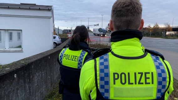Zwei Polizisten stehen an einer Straße und messen die Geschwindigkeit vorbeifahrender LKWs. © NDR Screenshot Foto: Screenshot