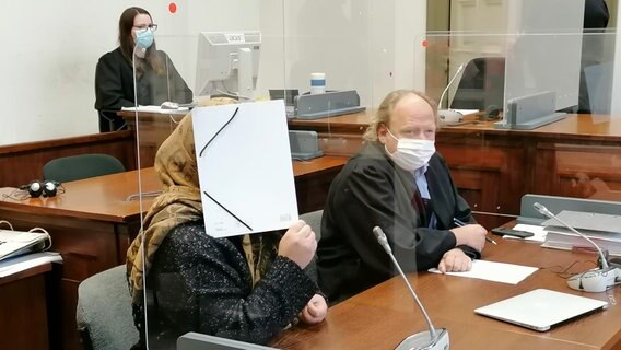 Die Angeklagte sitzt im Gerichtssaal und verdekt ihr Gesicht mit einem Aktenordner. © NDR Foto: Elke Spanner