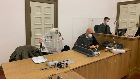 In einem Hamburger Gerichtssaal verdeckt sich eine Angeklagte mit einer Zeitung das Gesicht. © NDR Foto: Elke Spanner