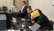 Ein 35-Jähriger, der wegen eines Verstoßes gegen das Waffengesetz angeklagt ist, hält sich im Gericht einen Briefumschlag vor das Gesicht. © NDR Foto: Elke Spanner