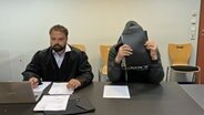 Ein Angeklagter in einem Prozess um Bilder von sexualisierter Gewalt gegen Kinder sitzt im Gerichtssaal neben seinem Anwalt. © NDR Foto: Elke Spanner