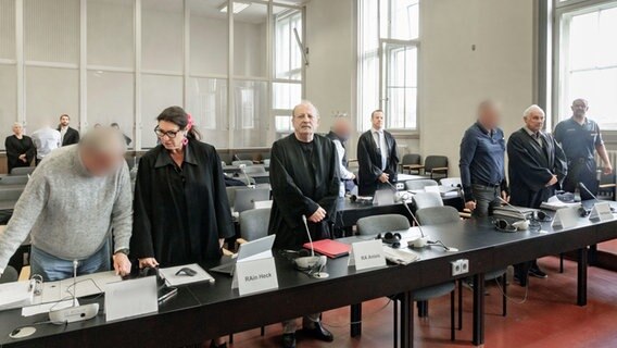 Vier Angeklagte stehen mit ihren Verteidigern in einem Gerichtssaal des Hamburger Landgerichts. Ihnen wird gemeinschaftliche Verabredung zum Verbrechen in Tateinheit mit unerlaubtem Erwerb einer Schusswaffe, Wohnungseinbruchdiebstahl und versuchter räuberischer Erpressung vorgeworfen. © picture alliance / dpa Foto: Markus Scholz