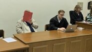 Ein Angeklagter verdeckt im Gerichtssaal sein Gesicht. © NDR Foto: Elke Spanner