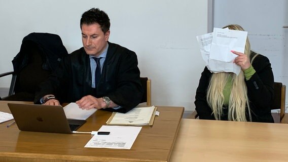 Eine Angeklagte versteckt sich hinter Zetteln und sitzt neben ihrem Anwalt im Gerichtssaal. © NDR Foto: Elke Spanner