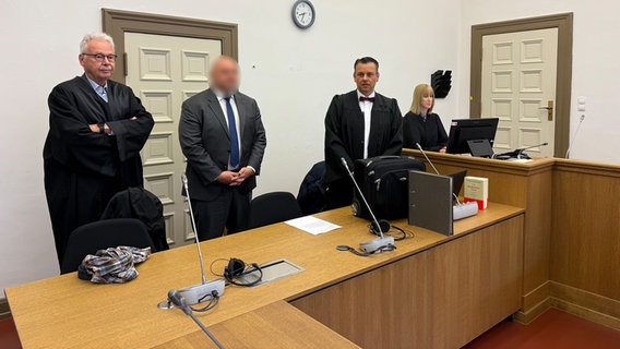 Anwälte und ein Angeklagter stehen in einem Gerichtssaal. © NDR / Elke Spanner Foto: Elke Spanner