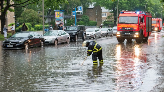 Eine Feuerwehrfrau steht im Stadtteil Öjendorf auf einer von starkem Regen überfluteten Straße. © picture alliance / dpa Foto: Daniel Bockwoldt
