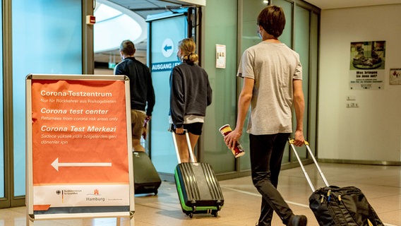 Reisende gehen aus dem Sicherheitsbereich des Hamburger Flughafens an einem Schild vorbei. © picture alliance/dpa Foto: Axel Heimken