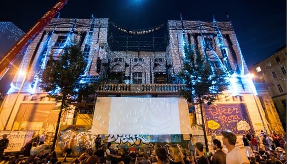 Zahlreiche Menschen sitzen und stehen am 15.08.2015 im Schanzenviertel in Hamburg während der einmaligen Performance des Musicals «Phantom der Oper» vor dem Kulturzentrum "Rote Flora". © dpa Foto: Daniel Bockwoldt