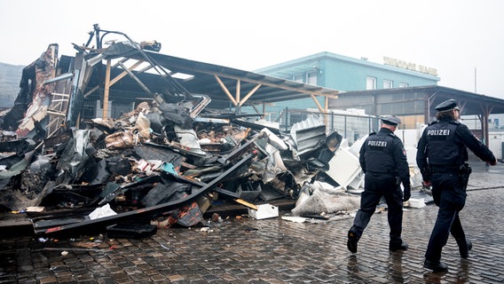 Zwei Polizisten gehen im Stadtteil Rothenburgsort an Brandschutt aus einer abgebrannten Lagerhalle vorbei. © dpa Foto: Daniel Bockwoldt