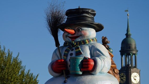 Ein Schneemann steht auf dem Dach einer Bude auf dem Heiligengeistfeld. Im Hintergrund ist die Kirschturmspitze der Hamburger Hauptkirche Sankt Michaelis Michel) zu sehen. © picture alliance/dpa Foto: Marcus Brandt