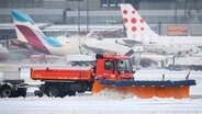 Ein Räumfahrzeug befreit die Landebahn am Hamburger Flughafen von Schnee während im Hintergrund ein Flugzeug enteist wird. © picture alliance / dpa 