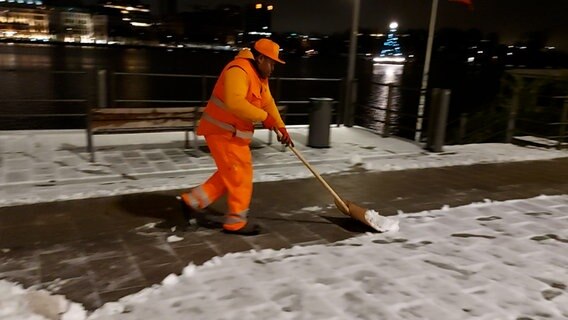 Ein Mitarbeiter der Stadtreinigung in Hamburg schiebt mit einem Schneeschieber Schnee von der Straße. © NDR Foto: Karsten Sekund