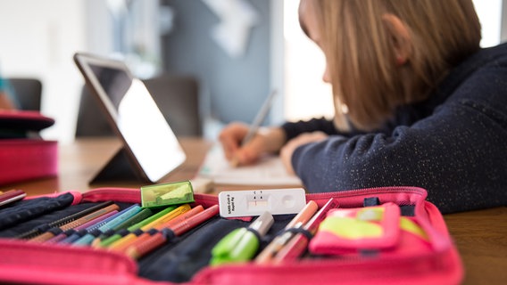 Eine Schülerin sitzt an einem Tisch auf der eine Federmappe mit einem negativen Corona-Schnelltest liegt. © picture alliance / Fotostand | Fotostand / K. Schmitt Foto: Fotostand / K. Schmitt