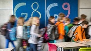 Schülerinnen und Schüler laufen an einer Tafel vorbei, auf der "G8" und "G9" steht. © picture alliance/dpa Foto: Armin Weigel