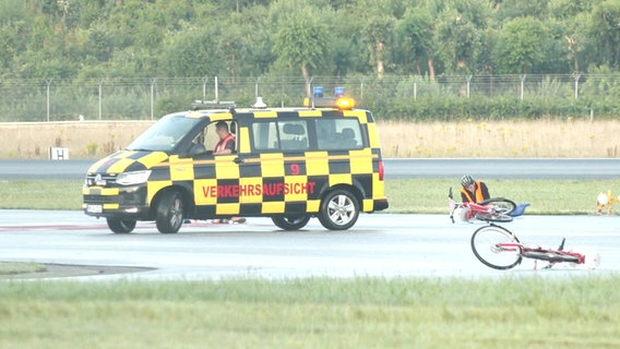 Ein Klimaaktivist sitzt festgeklebt auf dem Rollfeld, daneben ein Fahrzeug des Flughafen. © Screenshot 