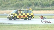 Ein Klimaaktivist sitzt festgeklebt auf dem Rollfeld, daneben ein Fahrzeug des Flughafen. © Screenshot 