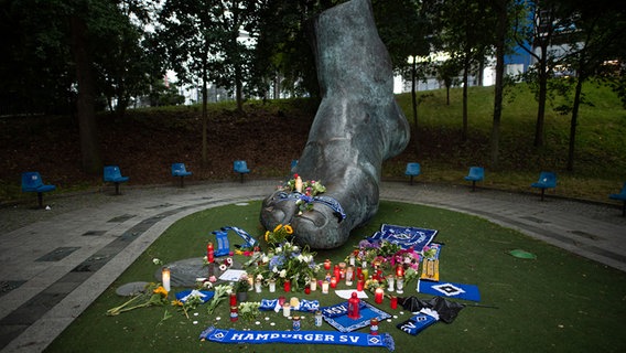 Auf und vor einer Bronze vor dem Volksparkstadion, die den Fuß des ehemaligen Fußballspielers Uwe Seeler darstellen soll, stehen und liegen Kerzen, Blumen und Schals. © picture alliance/dpa | Daniel Reinhardt Foto: Daniel Reinhardt