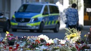 Blumen und Kerzen sind in Solingen zu sehen, dahinter ein Polizeiwagen. Bei einem Stadtfest waren dort drei Menschen mit einem Messer getötet worden. © picture alliance / dpa Foto: Federico Gambarini