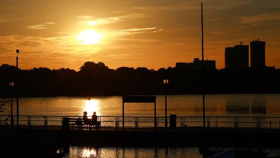 Zwei Menschen sitzen bei Sonnenaufgang auf einer Bank am Anleger Rabenstraße an der Alster. © picture alliance/dpa Foto: Christian Charisius