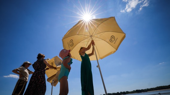 Mehrere Frauen stellen in Hamburg Sonnenschirme am Elbstrand auf. © picture alliance / dpa Foto: Christian Charisius
